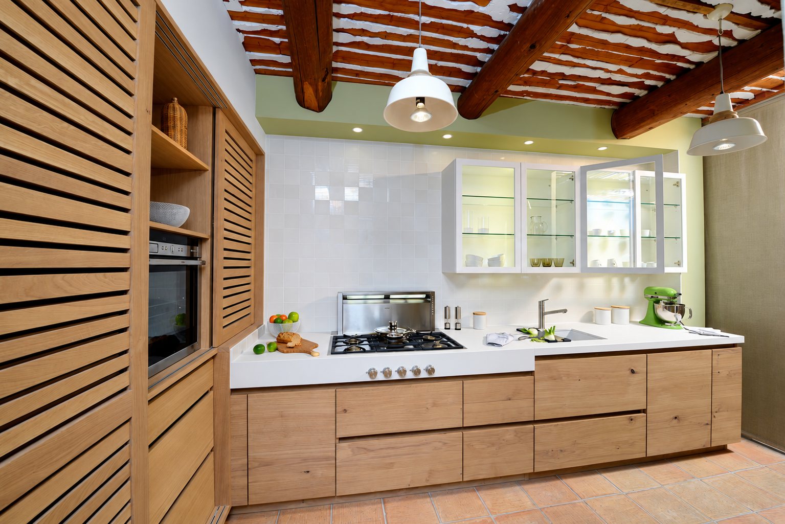 Cuisine sur mesure en bois clair avec plan de travail blanc, plaque de cuisson à gaz, placards à claires-voies et plafond à poutres apparentes.