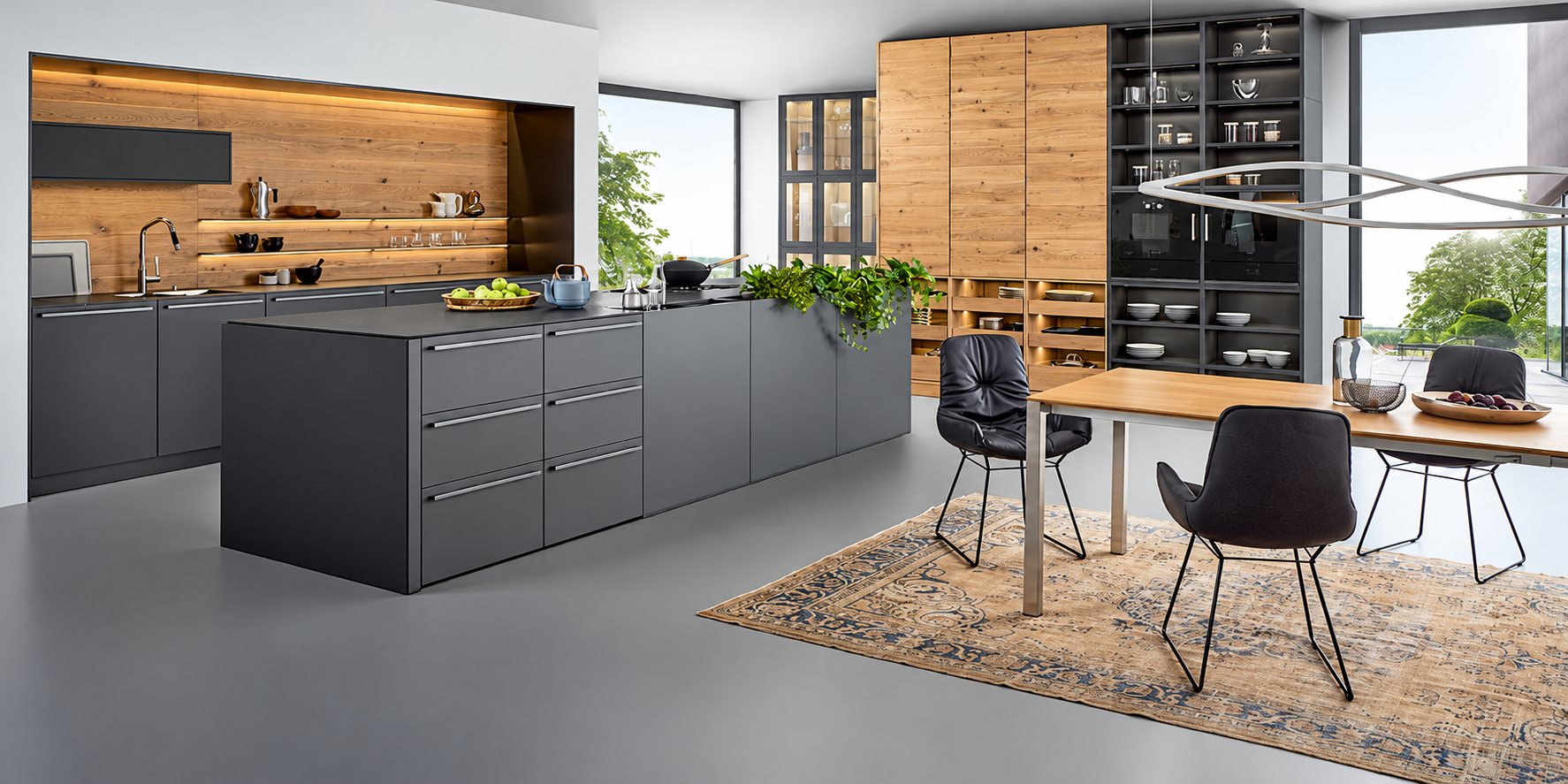 Cuisine contemporaine aux façades anthracite mates et panneaux de bois clair, avec grand îlot central, table en bois, chaises noires et tapis ancien.