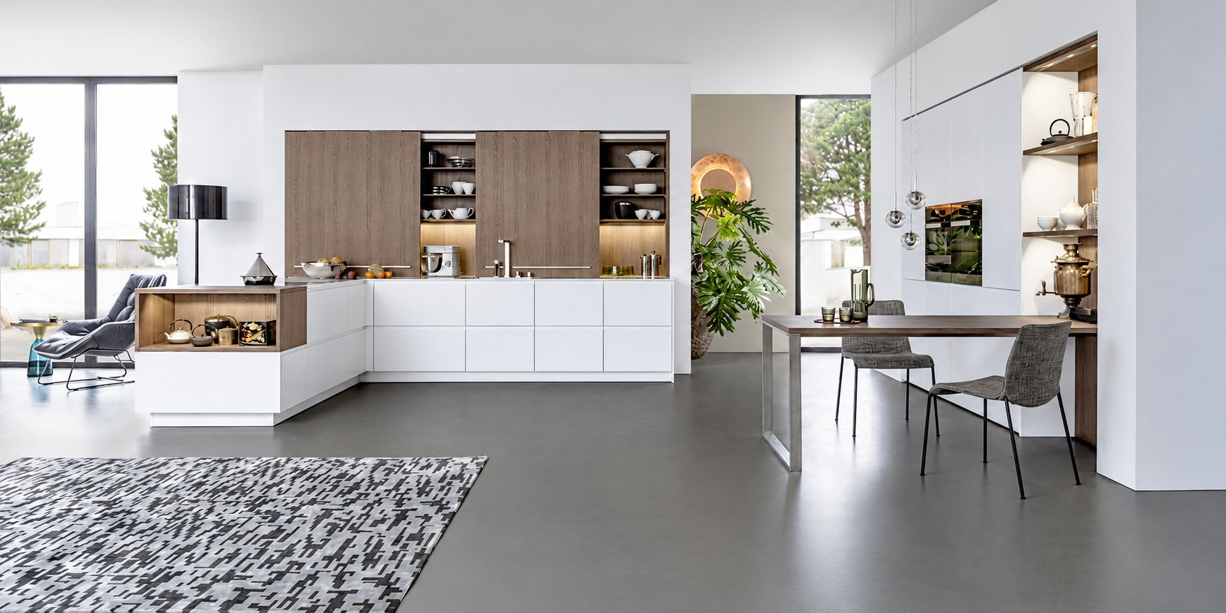 Grande cuisine contemporaine aux façades blanches et bois, avec îlot d'angle, table haute, chaises grises et sol en béton ciré gris.