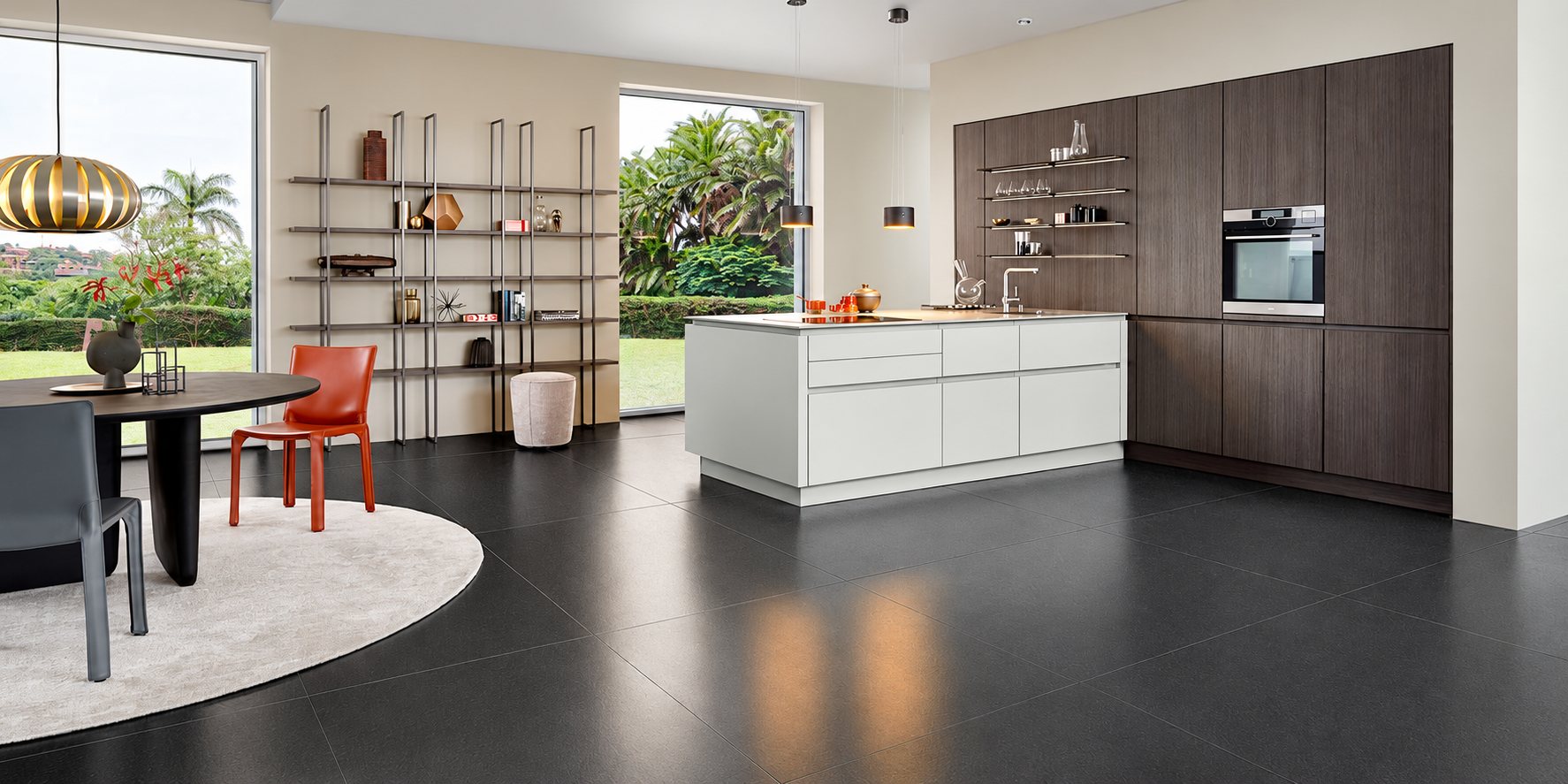 Cuisine contemporaine ouverte avec îlot central blanc, façades en bois foncé, four encastré, étagères métalliques et table ronde au premier plan.