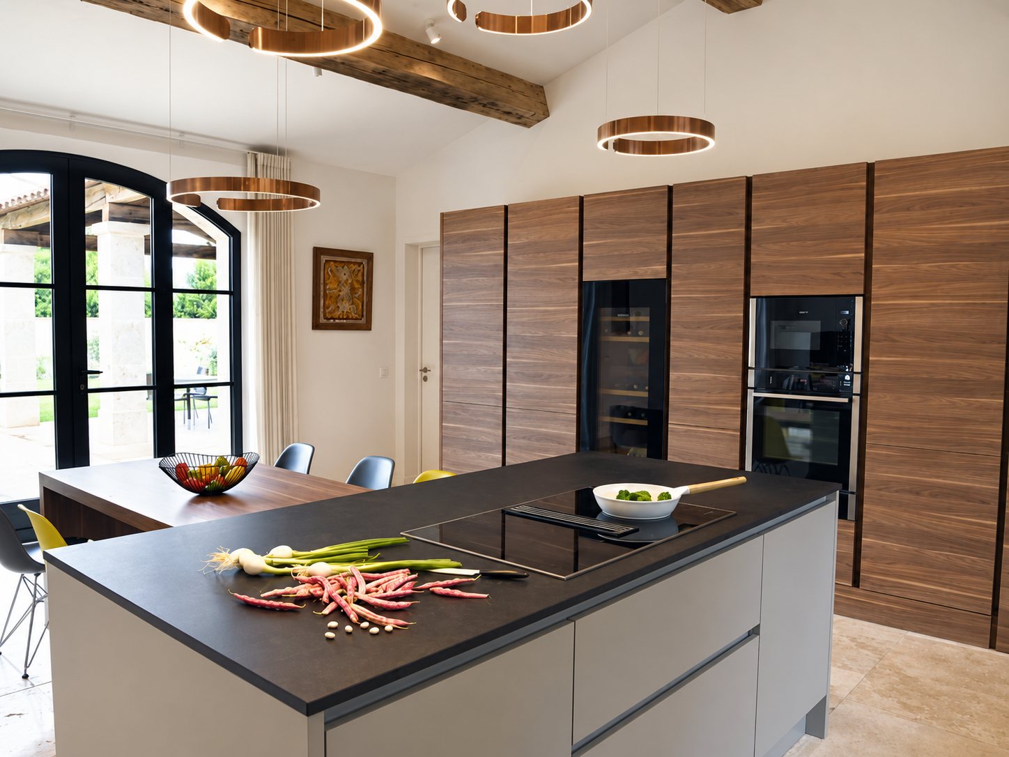 Cuisine contemporaine lumineuse avec grand îlot à plaque de cuisson, hautes armoires en bois, suspensions cuivrées et baie vitrée cintrée.
