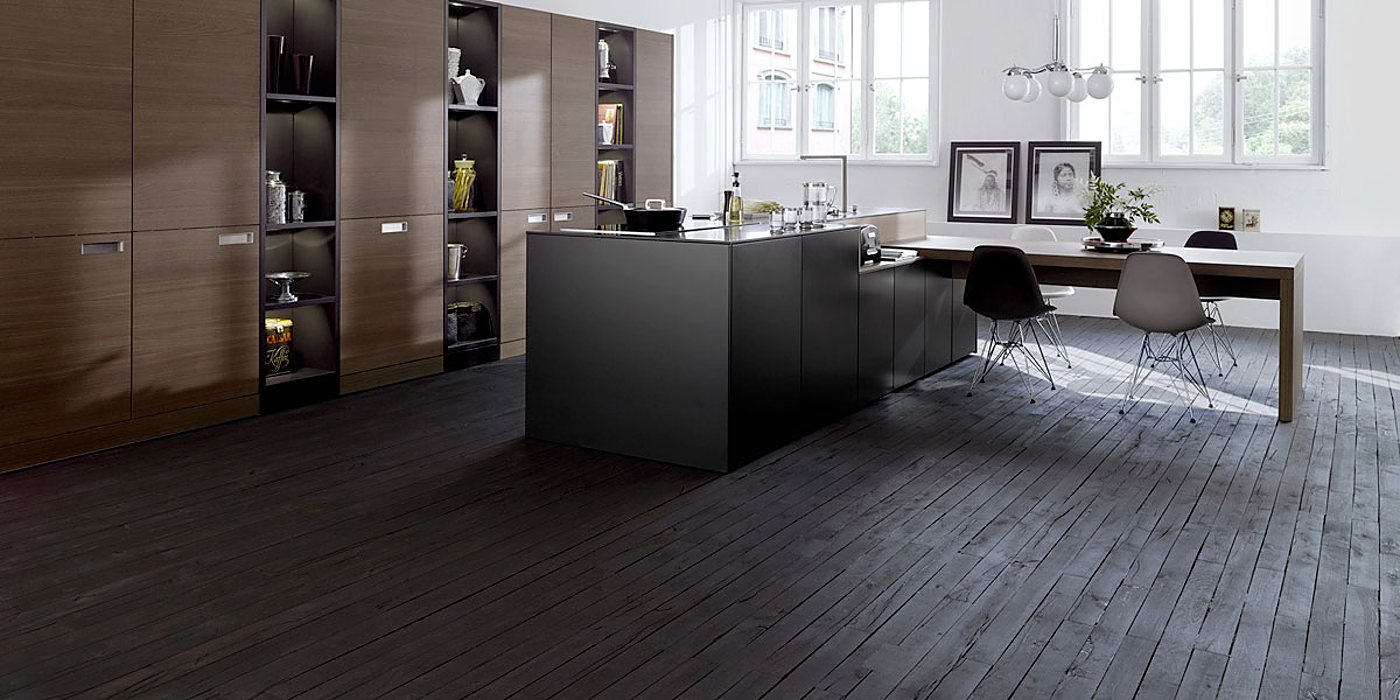Cuisine contemporaine lumineuse avec îlot central noir, hauts placards en bois foncé, table à manger prolongée et sol en parquet noir.