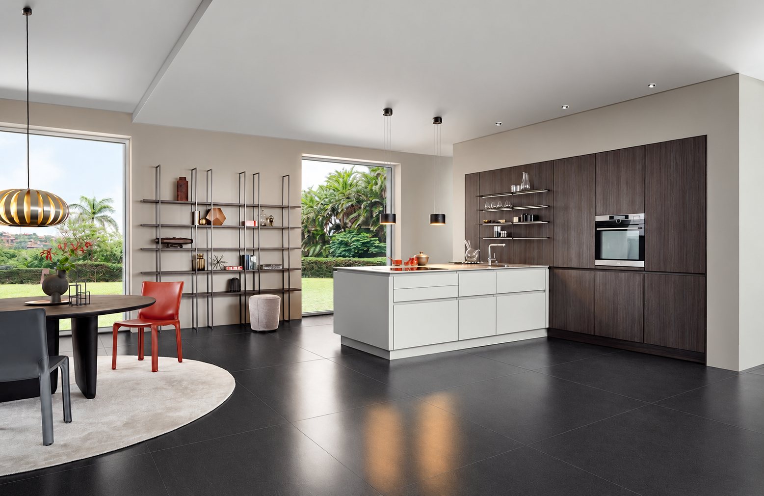 Cuisine contemporaine avec îlot clair, meubles en bois foncé, four encastré, étagères métalliques et salle à manger ouvrant sur un jardin.