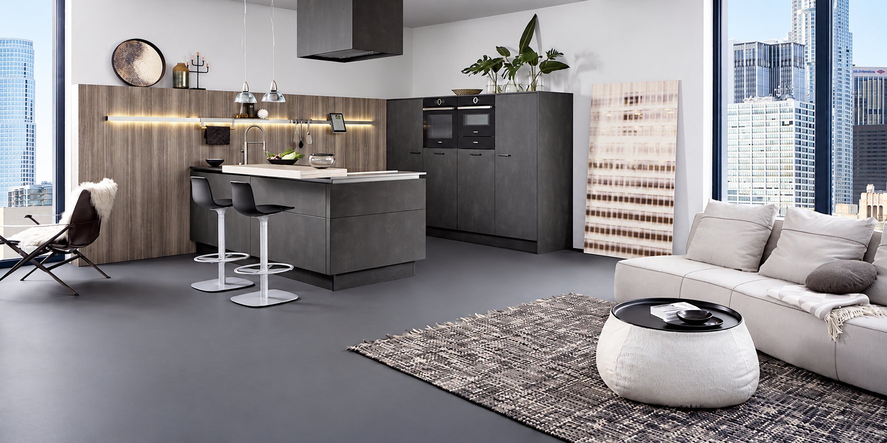 Cuisine contemporaine grise et bois avec îlot et tabourets, ouverte sur un salon avec canapé clair et grandes baies vitrées donnant sur la ville.